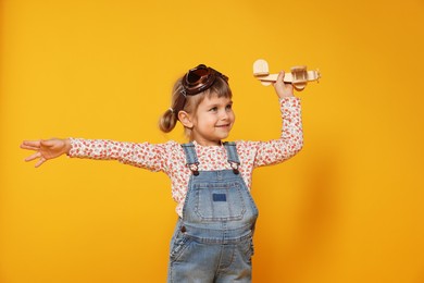 Photo of Happy little girl playing with toy plane on orange background