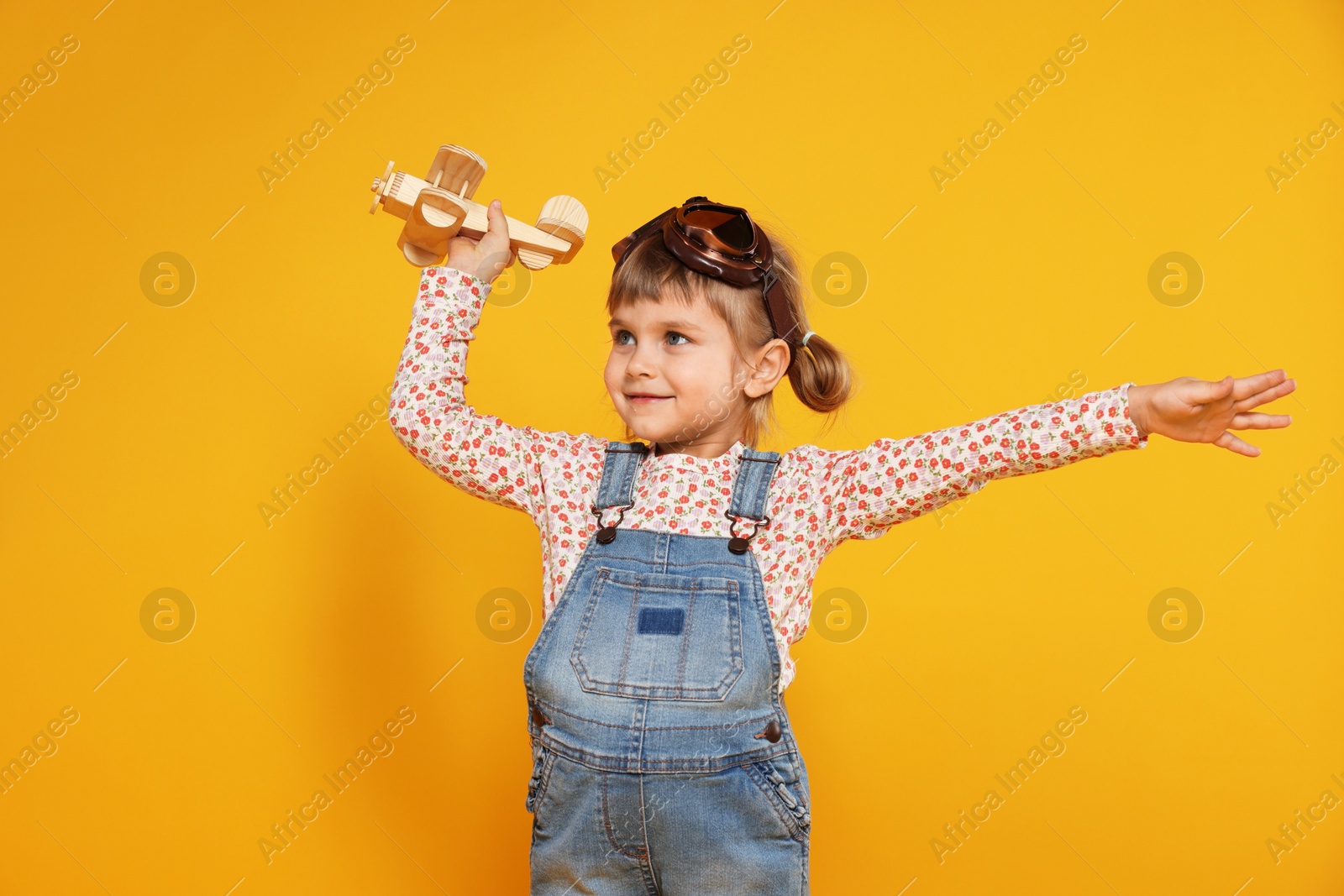 Photo of Cute little girl playing with toy plane on orange background