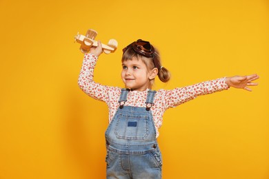 Photo of Cute little girl playing with toy plane on orange background