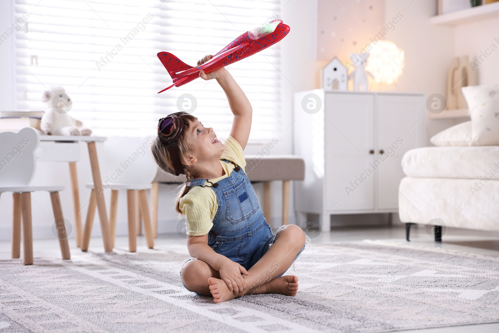 Photo of Cute little girl playing with toy plane at home