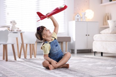 Photo of Cute little girl playing with toy plane at home