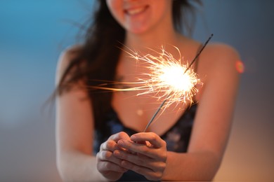 Photo of Woman with bright burning sparkler on color background, selective focus