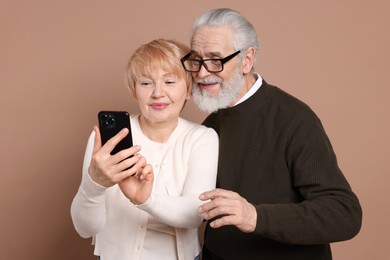 Photo of Lovely senior couple looking at smartphone on beige background