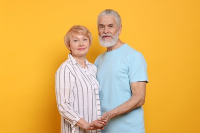 Photo of Portrait of lovely senior couple holding hands on orange background