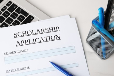 Photo of Scholarship application form, pens and laptop on white marble table, above view