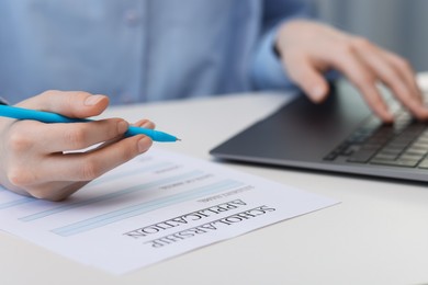 Photo of Student filling scholarship application form while using laptop at white table, closeup