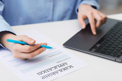 Photo of Student filling scholarship application form while using laptop at white table, closeup