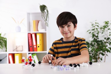 Photo of Boy making DNA structure model at desk indoors. Space for text