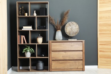 Photo of Shelving unit with decor, chest of drawers and folding screen near grey wall indoors