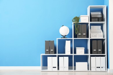 Photo of Shelving unit with folders and globe near light blue wall indoors, space for text