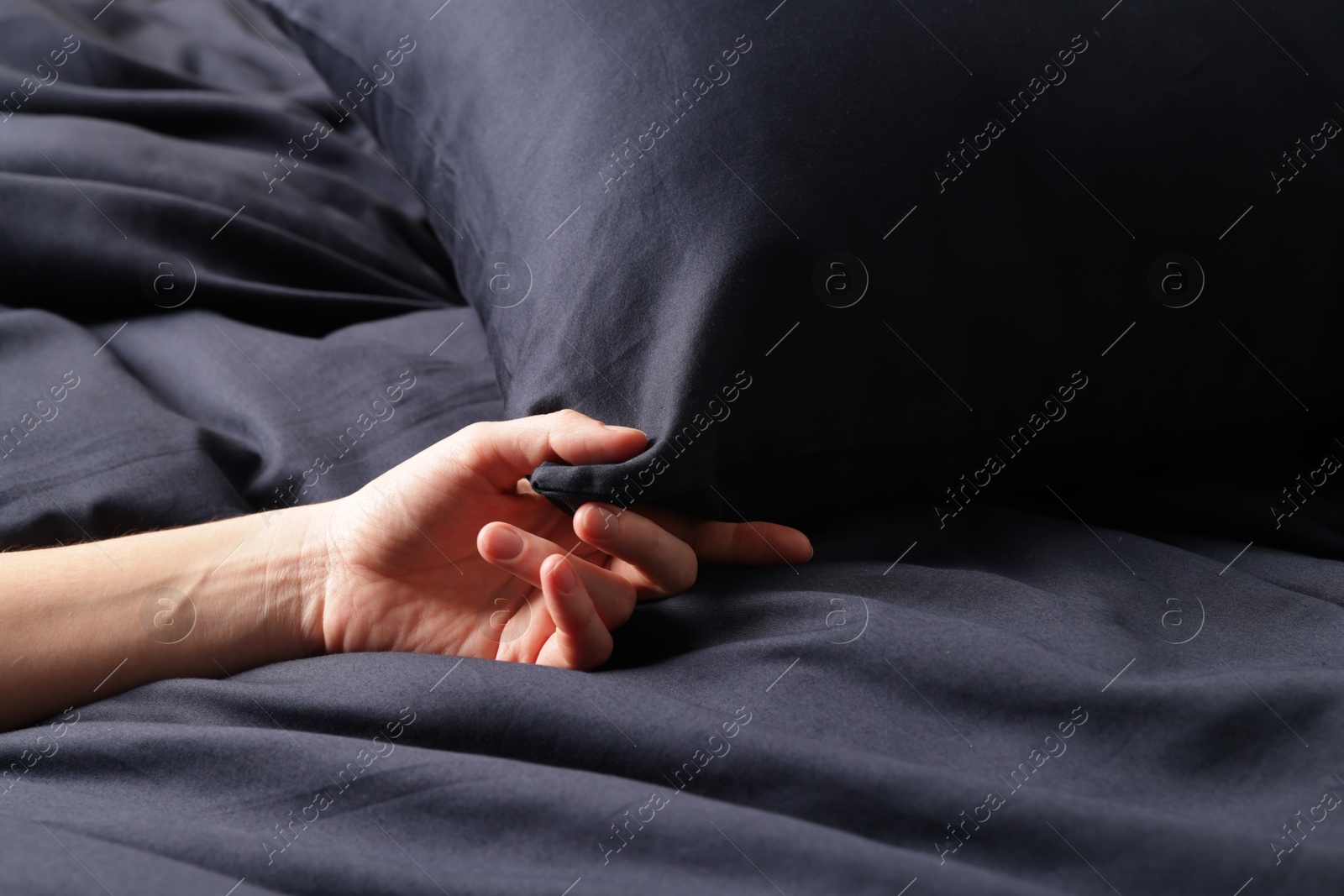 Woman touching dark blue silk linens on bed, closeup Photo of Woman touching dark blue silk linens on bed, closeup