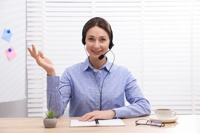 Photo of Smiling online speaker in headset streaming webinar at table indoors, view from web camera