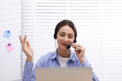 Photo of Smiling online speaker in headset streaming webinar with laptop indoors