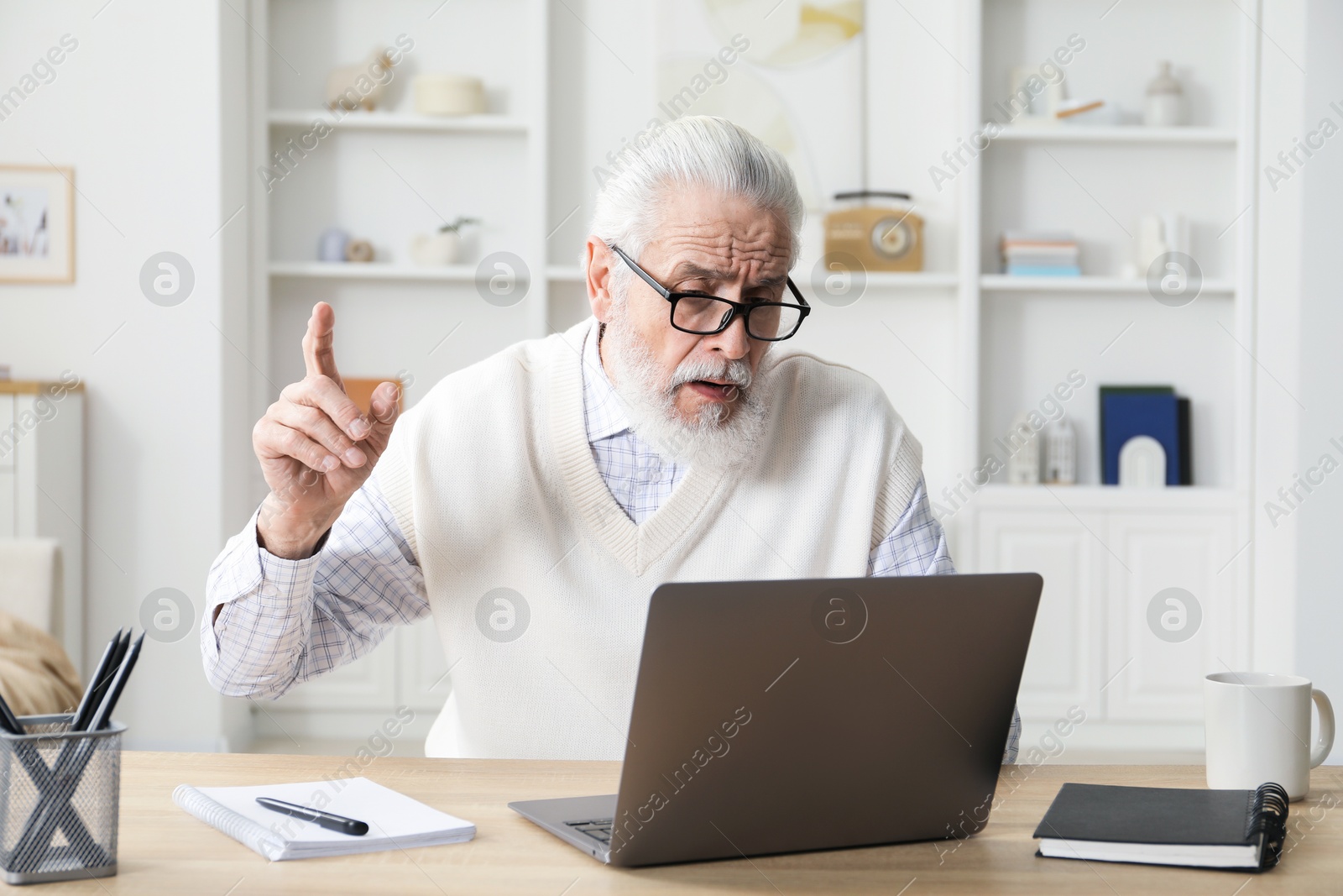 Photo of Senior man learning online using laptop at desk indoors. Self-study