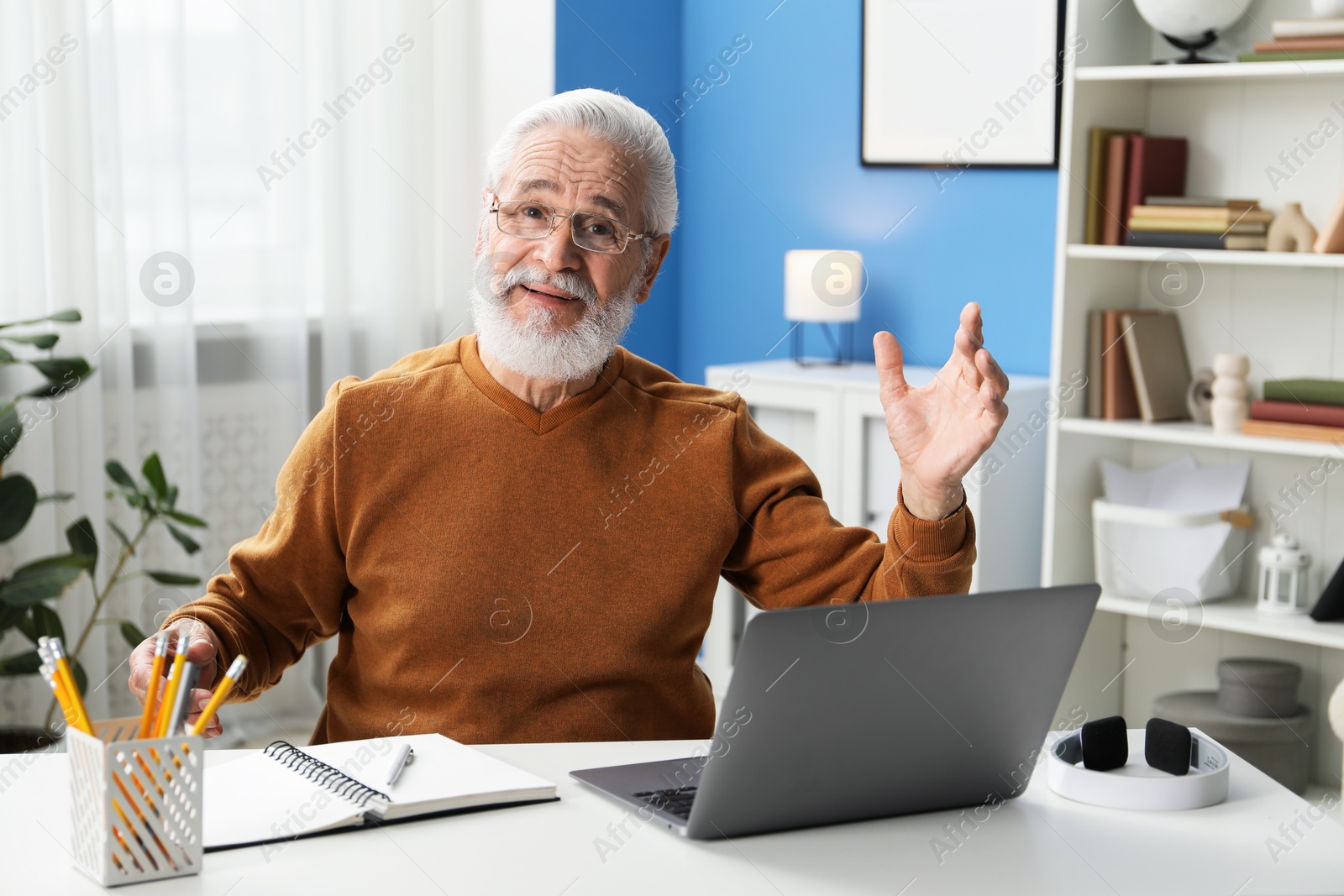 Photo of Senior man learning online using laptop at desk indoors. Self-study