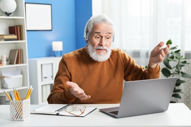 Photo of Senior man having online lesson with teacher at desk indoors. Self-study