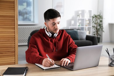 Photo of Man taking notes during online lesson at desk indoors. Self-study