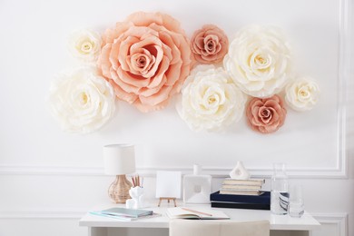 Photo of Beautiful decorative paper flowers on white wall above desk indoors