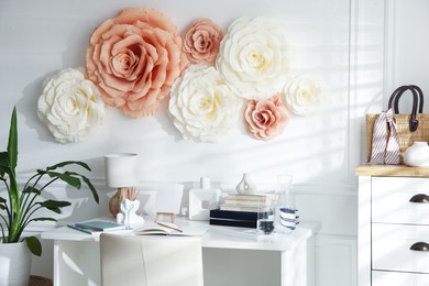 Photo of Beautiful decorative paper flowers on white wall and stylish furniture indoors