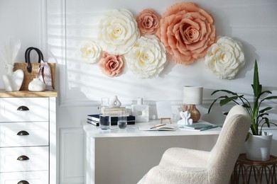 Photo of Beautiful decorative paper flowers on white wall and stylish furniture indoors