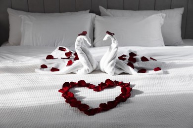 Photo of Heart of beautiful rose petals and swans made with towels on bed indoors