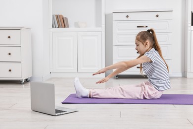 Photo of Little girl exercising near laptop at home. Morning routine