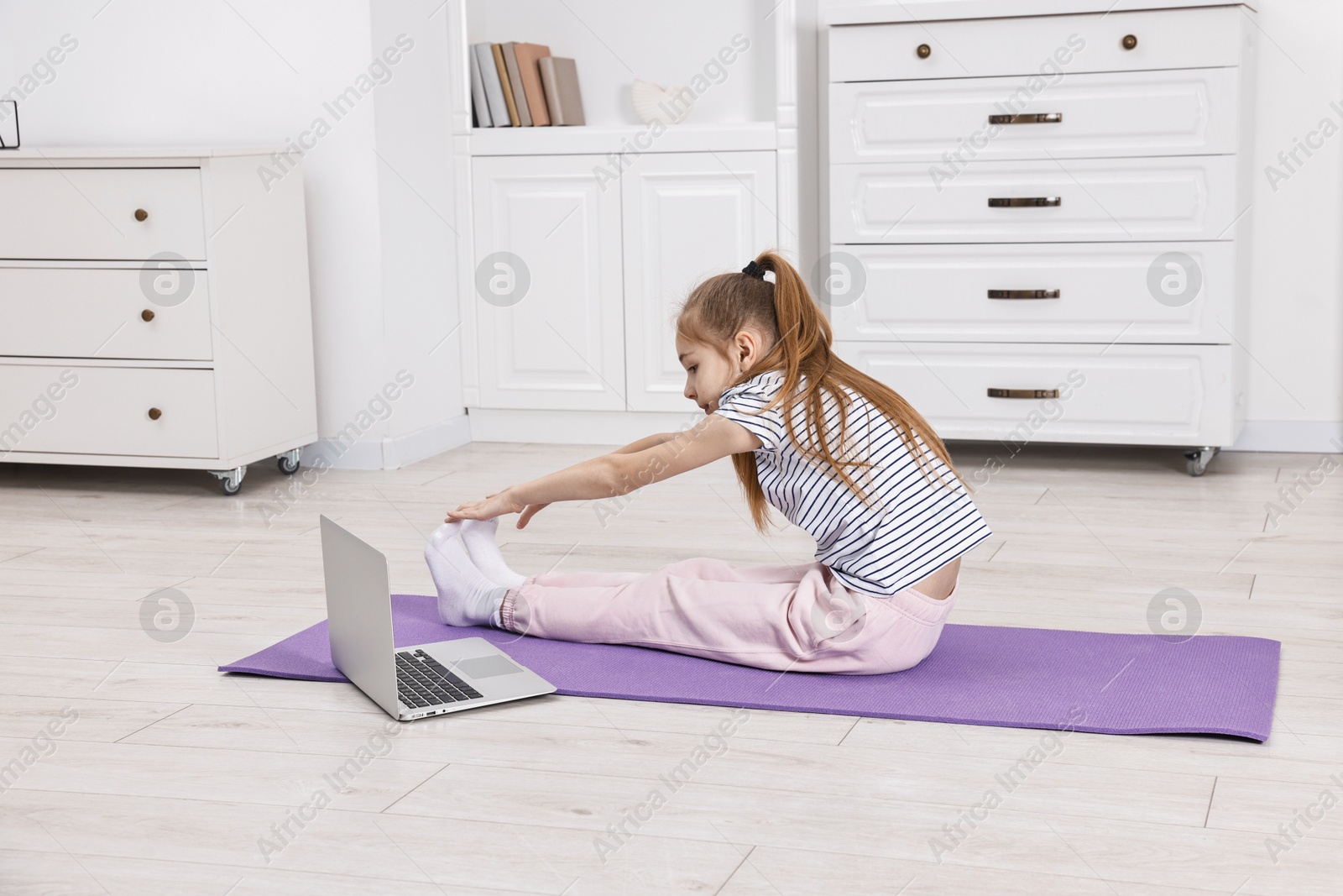 Photo of Little girl exercising near laptop at home. Morning routine