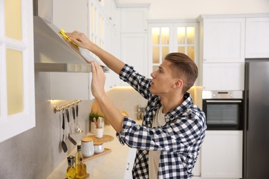 Photo of Man cleaning kitchen hood with rag at home