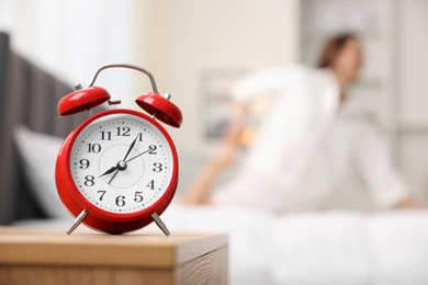 Photo of Young woman exercising on bed at home, focus on alarm clock. Morning routine