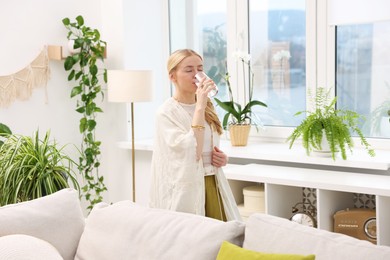 Photo of Feng shui. Young woman drinking water near houseplants at home