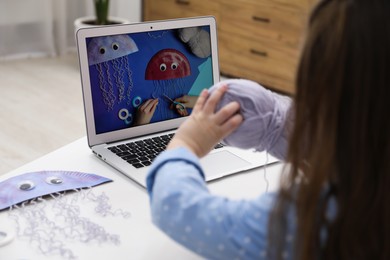 Photo of Little girl making handmade jellyfish by craft tutorial video at home, selective focus. Child creativity