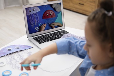 Photo of Little girl making handmade jellyfish by craft tutorial video at home, selective focus. Child creativity