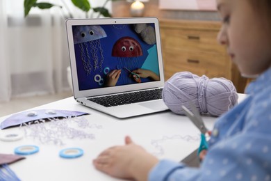 Photo of Little girl making handmade jellyfish by craft tutorial video at home, selective focus. Child creativity