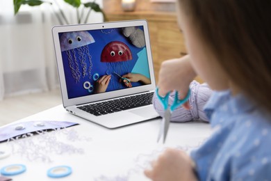 Photo of Little girl making handmade jellyfish by craft tutorial video at home, selective focus. Child creativity