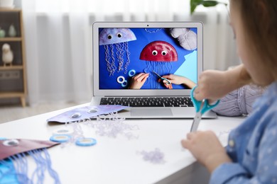 Photo of Little girl making handmade jellyfish by craft tutorial video at home, selective focus. Child creativity