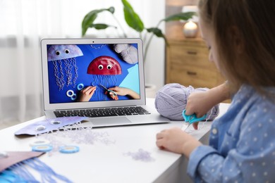 Photo of Little girl making handmade jellyfish by craft tutorial video at home, selective focus. Child creativity