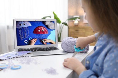 Photo of Little girl making handmade jellyfish by craft tutorial video at home, selective focus. Child creativity