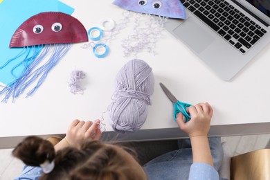 Photo of Little girl making handmade jellyfish by craft tutorial video at white table, top view. Child creativity