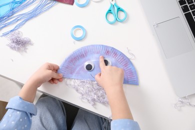 Photo of Little girl making paper jellyfish at white table, top view. Child handmade craft