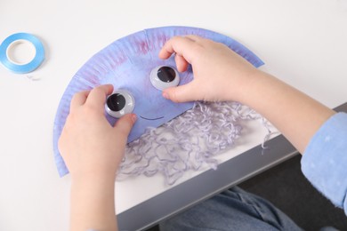 Photo of Little girl making paper jellyfish at white table, closeup. Child handmade craft