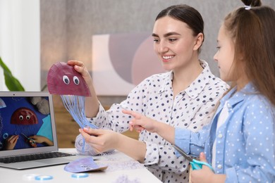 Photo of Woman and little girl making handmade jellyfish by craft tutorial video at home. Child creativity