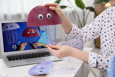 Photo of Woman making handmade jellyfish by craft tutorial video at home, closeup. Child creativity