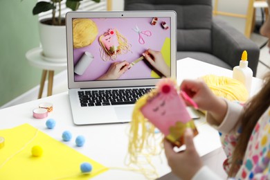 Photo of Little girl making handmade toy by following craft tutorial video at home. Child creativity