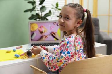 Photo of Little girl making handmade toy by following craft tutorial video at home. Child creativity