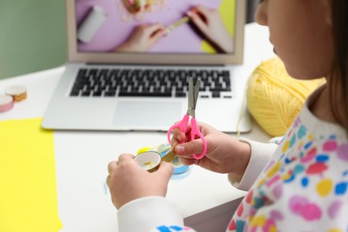 Photo of Little girl making handmade toy by following craft tutorial video at home, closeup. Child creativity