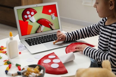 Photo of Little girl making handmade fly agaric by following craft tutorial video at home. Child creativity