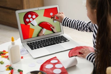 Photo of Little girl making handmade fly agaric by following craft tutorial video at home. Child creativity