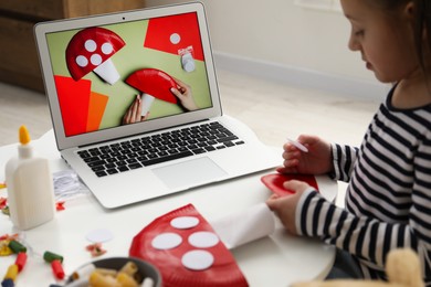 Photo of Little girl making handmade fly agaric by following craft tutorial video at home. Child creativity