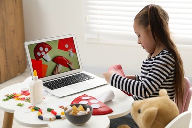 Photo of Little girl making handmade fly agaric by following craft tutorial video at home. Child creativity