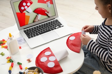 Photo of Little girl making handmade fly agaric by following craft tutorial video at home. Child creativity